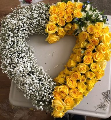 Heart-shaped arrangement of yellow roses and baby’s breath flowers.