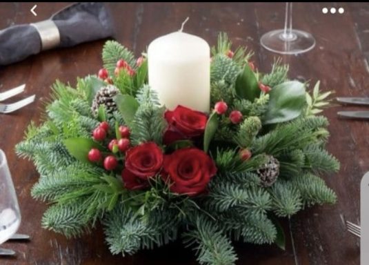 A floral Christmas centrepiece with red roses, berries, and a white candle.