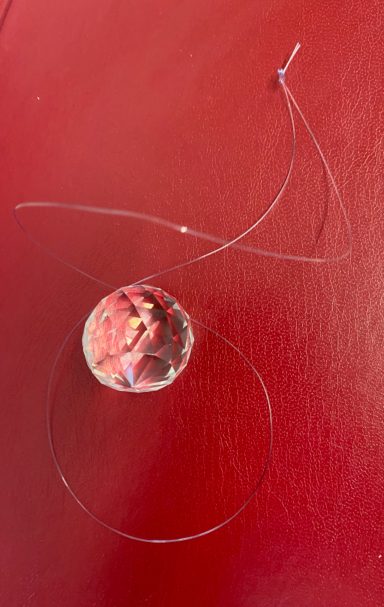 Glass marble with a thread looped around it on a red background.