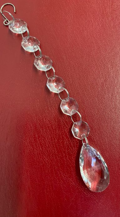 Clear crystal drop pendant with multiple round links on a red background.