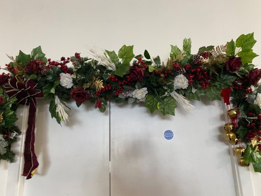 A decorative garland with holly, berries, and a bow, suitable for festive occasions.