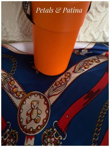 An orange cup atop a patterned blue surface featuring ornate details.