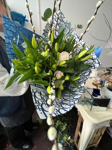 A floral bouquet with green leaves and white flowers, wrapped in blue and patterned paper.