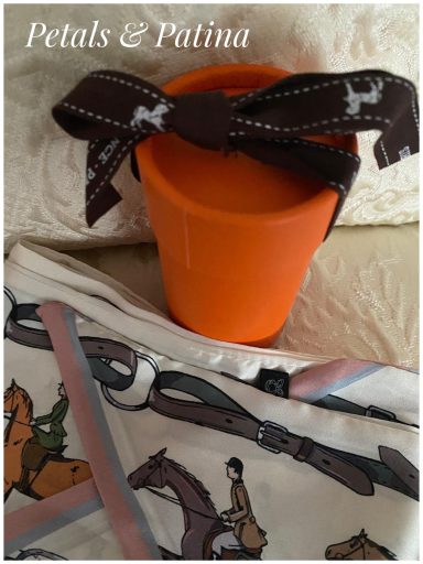 Orange pot with a brown ribbon tied around it, set against a patterned cloth.