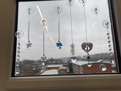 Colourful glass ornaments hang from a window, overlooking a cloudy cityscape.