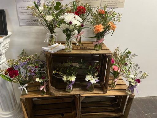 A wooden display featuring various flower arrangements in jars and vases.