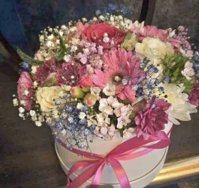 A pastel flower arrangement in a round box, adorned with a pink ribbon.