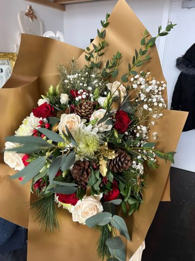 A floral bouquet with red roses, white flowers, pinecones, and greenery on kraft paper.