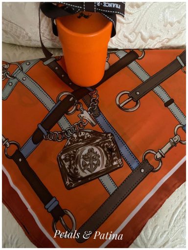 Orange cup beside a patterned scarf featuring straps and a decorative pendant.