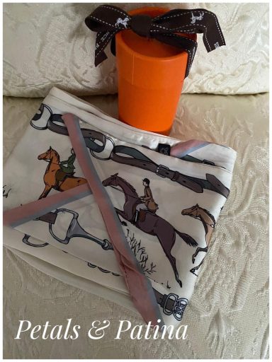 A folded horse-themed blanket next to an orange bucket and a scarf.