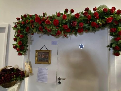 Decorative floral arrangement of red roses above a closed door with a framed picture.